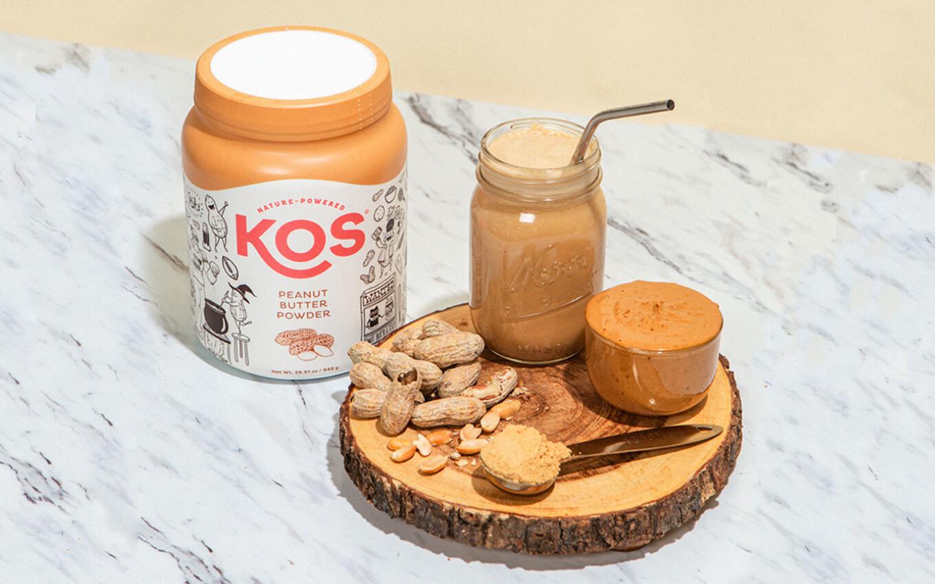 Container of KOS' peanut butter powder next to a peanut butter based smoothie