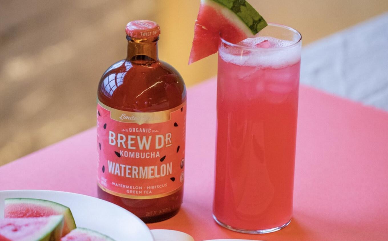Glass bottle of Brew Dr Kombucha's watermelon flavour next to glass filled with it and watermelon slices