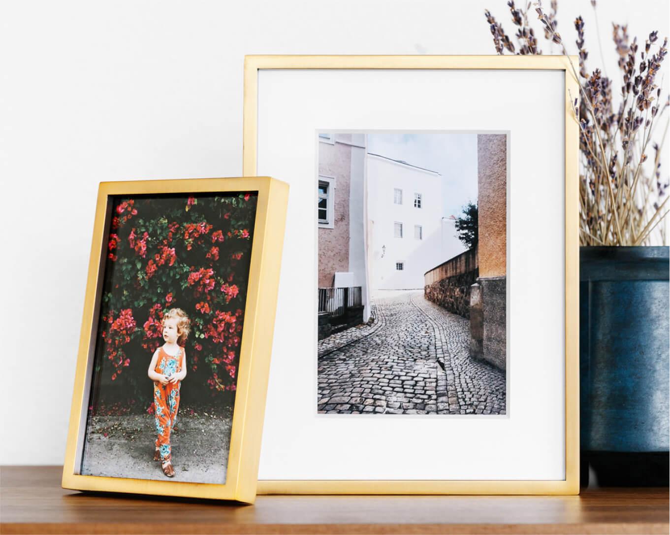 Artifact Uprising wood photo frames on a table showing a photo of a small child in front of flowers and a photo of a cobblestone road