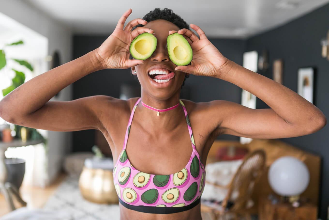 Woman wearing a MeUndies bra with an avocado pattern, holding two avocado halfs over her eyes and making a silly face